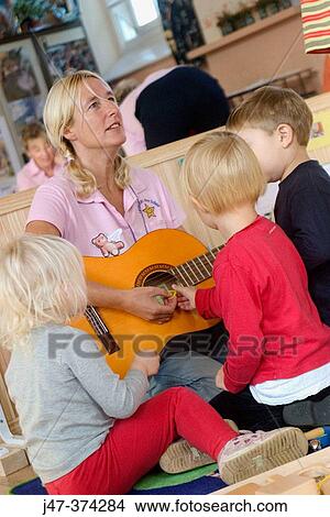 Nursrey school teacher, playing a guitar to a small group of children (3-4 year olds) View Large Photo Image Picture - Nursrey school teacher, playing a guitar to a small group of children (3-4 year olds). Fotosearch