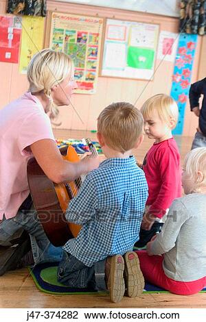 Stock Image - Nursrey school teacher, playing a guitar to a small group of children (3-4 year olds). Fotosearch
