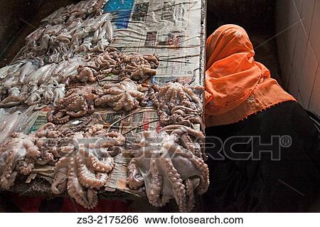 Stock Photograph - Octopus lying on the bench with the vendor wearing headscarf by side at the daily market on Darajani road, Stone Town, Unguja Island, Zanzibar Archipelago, Tanzania, East Africa.. Fotosearch