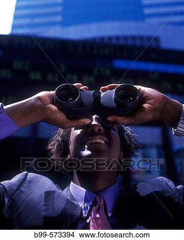 Office worker looking through binoculars below stock market ticker display. View Large Photo Image Picture - Office worker looking through binoculars below stock market ticker display.. Fotosearch