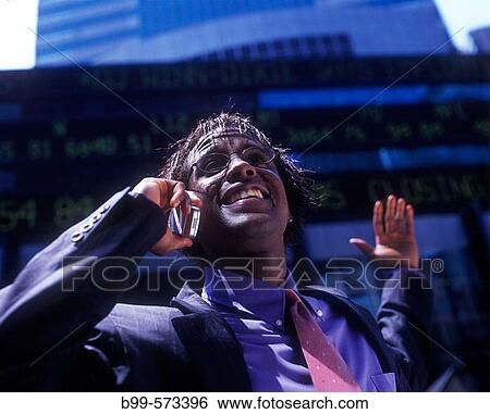 Stock Photograph - Office worker with telephone, Below stock market ticker display.. Fotosearch