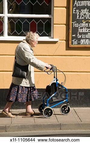 Old elderly woman walking on street with mobility aid - three wheeler shopping buggy View Large Photo Image Picture - Old elderly woman walking on street with mobility aid - three wheeler shopping buggy. Fotosearch