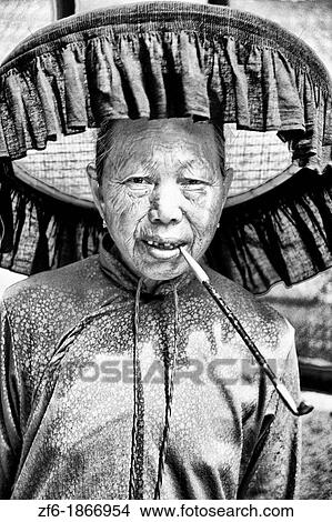 Picture - Old Hakka woman with pipe in the old walled city of Kam Tin in the New Territories area of Hong Kong This is a dying breed of woman for tourists with black hats and black clothes with smoking. Fotosearch