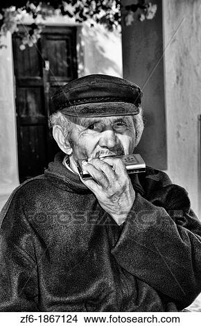 Old local man playing harmonica in beautiful village of Oia in Santorini in Greek Islands in Greece Europe View Large Photo Image Picture - Old local man playing harmonica in beautiful village of Oia in Santorini in Greek Islands in Greece Europe. Fotosearch