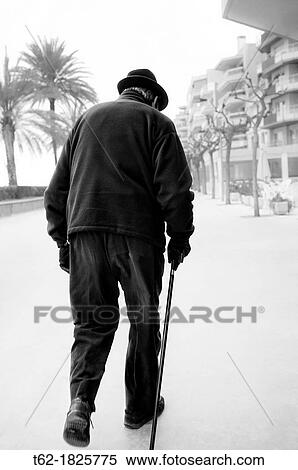Stock Photography - Old man walking alone along the promenade by the sea on a gray day. Fotosearch