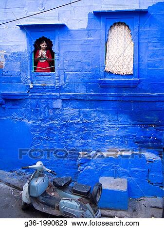 Stock Photo - Old scooter parked next to a building, smiling girl looking out through window in Jodhpur, Rajasthan, India.. Fotosearch