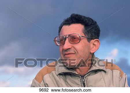 Older dark-haired man outdoors in warm jacket looking off into distance against dramatically cloudy sky View Large Photo Image Stock Image - Older dark-haired man outdoors in warm jacket looking off into distance against dramatically cloudy sky. Fotosearch