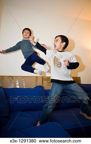 Stock Image - Older male child repelling a kung-fu attack by his younger brother during domestic play fighting on the sofa. Fotosearch