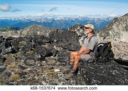 Picture - older man sitting on top of a mountain peak in the Cayoosh Range, British Columbia, Canada.. Fotosearch