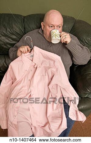 Picture - Older man with a pink shirt and coffee cup in his hands. Fotosearch