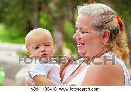Older woman in her 60s proudly holding her baby grandchild View Large Photo Image Stock Photo - Older woman in her 60s proudly holding her baby grandchild. Fotosearch