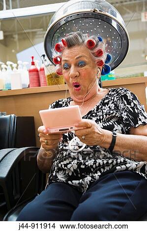 Older woman with video game and headphones in hair salon View Large Photo Image Picture - Older woman with video game and headphones in hair salon. Fotosearch
