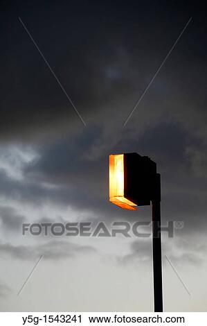 Stock Image - one lit light bulb outdoors in dark grey sky. Fotosearch