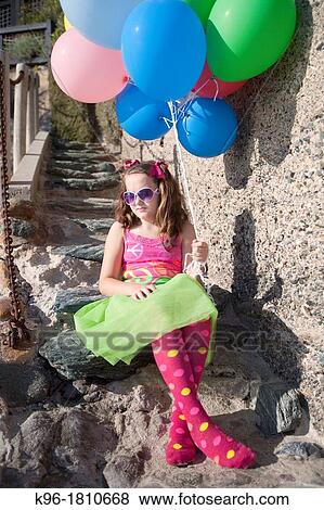 Stock Photo - one little girl sitting on stone steps holding balloons. Fotosearch