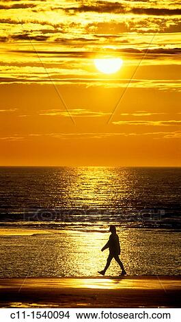 one single man walking along beach at sunset with sea and sun behind View Large Photo Image Picture - one single man walking along beach at sunset with sea and sun behind. Fotosearch