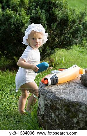 Stock Photograph - One Year Old Baby Girl Standing Outside with Toys. Fotosearch
