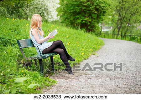 One young attractive woman sitting on bench in a park writing in a diary. View Large Photo Image Stock Photo - One young attractive woman sitting on bench in a park writing in a diary.. Fotosearch