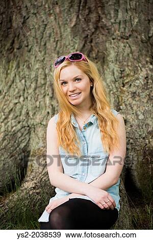 Stock Photo - One young blonde attractive woman in front of big tree in a park.. Fotosearch