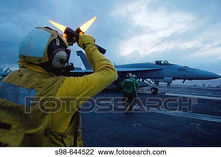 Stock Image - PACIFIC OCEAN, (June 22, 2006) - An Aircraft director instructs the pilot of an F/A-18 Super Hornet to hold his position while awaiting launch off the flight deck of USS Kitty Hawk (CV 63) during night-time flight operations.. Fotosearch