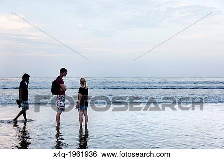 Palolem, India-September 1, 2012. A couple of tourists chatting on the shore as the tide rises and the sky begins to sunset. View Large Photo Image Stock Photograph - Palolem, India-September 1, 2012. A couple of tourists chatting on the shore as the tide rises and the sky begins to sunset.. Fotosearch