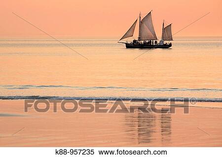 Stock Photography - Pearl lugger cruising past Cable beach at sunset. Broome, Western Australia.. Fotosearch