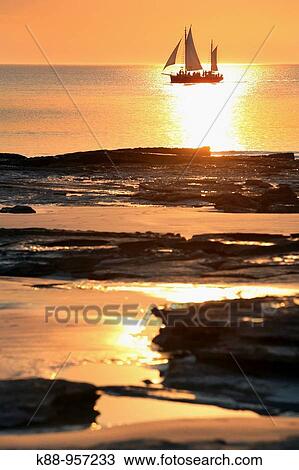 Stock Image - Pearl luggers cruising past Cable beach at sunset. Broome, Western Australia.. Fotosearch