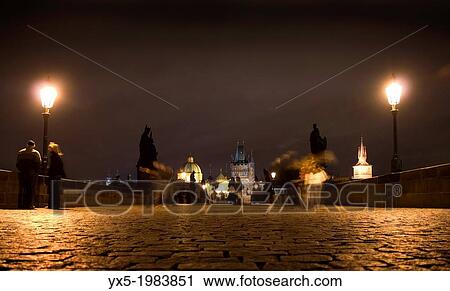 Stock Image - Pedestrian walking on Charles Bridge in Prague at night.. Fotosearch