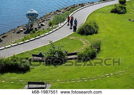 Stock Image - pedestrians walk on the path on the north side of False Creek, Vancouver, BC, Canada.. Fotosearch