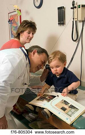 Pediatrician / physician examining young boy with otoscope in medical office with mother looking on View Large Photo Image Picture - Pediatrician / physician examining young boy with otoscope in medical office with mother looking on. Fotosearch