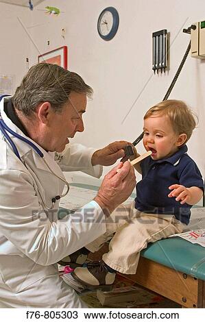 Pediatrician / physician examining young boy with tongue depressor in medical office View Large Photo Image Stock Image - Pediatrician / physician examining young boy with tongue depressor in medical office. Fotosearch
