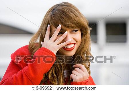 Stock Image - Peeking and smiling through fingers pretty woman portrait. Fotosearch