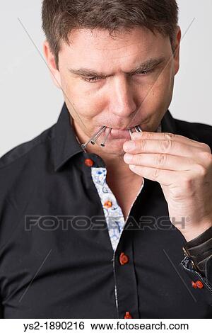 Stock Photograph - Pensive adult male holds metallic nails in his mouth. Fotosearch