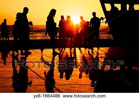 Stock Photograph - People enjoying the sunset on a warm summer evening at the Sun Salutation on the ground in Zadar, Croatia Designed by architect Nikola Basic, it harvests sun during the day and puts on a light show in the evening using the rhythm of the waves. Fotosearch
