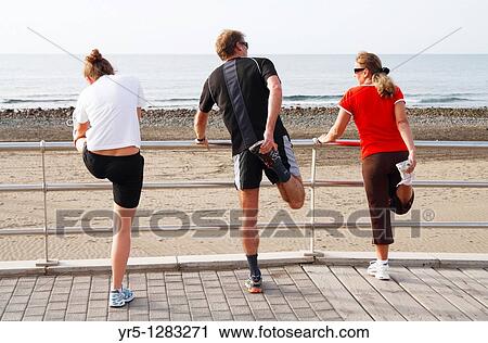 Stock Image - People stretching before running on beach in Spain. Fotosearch
