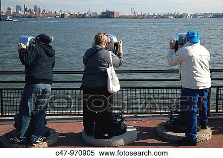 Stock Photography - People using coin-operated binocular viewer installed at the Statue of Liberty overviewing Lower Manhattan, New York, USA. Fotosearch