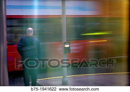 Stock Image - Person above a sidewalk waiting to cross while passing a bus on a street in London. Fotosearch
