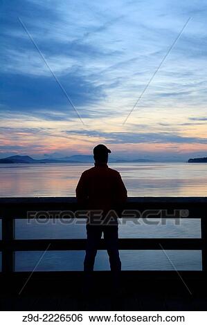Stock Photograph - Person on fishing pier at dawn, Sidney, British Columbia.. Fotosearch