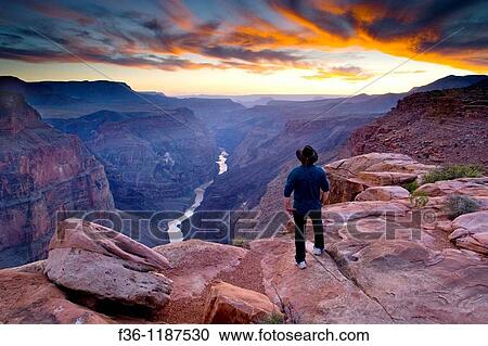 Stock Image - Person standing at the edge of steep rugged cliffs above the Colorado River at sunset, Toroweap, Grand Canyon National Park, Arizona. Fotosearch