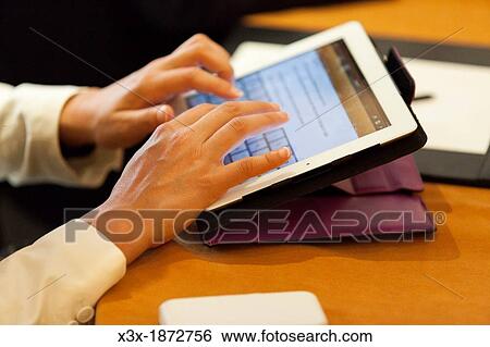 Stock Photograph - Person typing on a tablet during a business meeting. Fotosearch