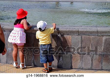 Peru, Lima, Miraflores, Malecon de la Reserva, Parque Salazar, urban park, fountain, water, stone ledge, Hispanic, boy, girl, child, standing on tiptoes, taller, shorter, height, red hat,. View Large Photo Image Stock Photograph - Peru, Lima, Miraflores, Malecon de la Reserva, Parque Salazar, urban park, fountain, water, stone ledge, Hispanic, boy, girl, child, standing on tiptoes, taller, shorter, height, red hat,.. Fotosearch
