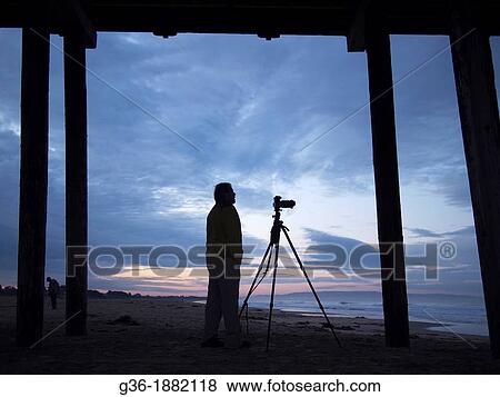 Stock Photo - Photographer under the pier and on the beach at sunrise in Pismo Beach, California. Fotosearch