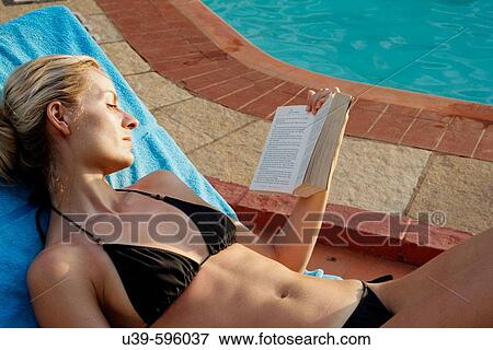 Picture of a blonde woman in a black bikini lying on a sunlounger by a pool and reading a book. View Large Photo Image Stock Photo - Picture of a blonde woman in a black bikini lying on a sunlounger by a pool and reading a book.. Fotosearch
