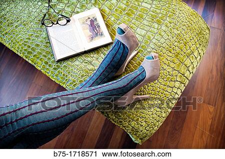 Stock Image - piernas de mujer con zapatos de tac? n relajada con un libro, female legs in high heels relaxed with a book. Fotosearch