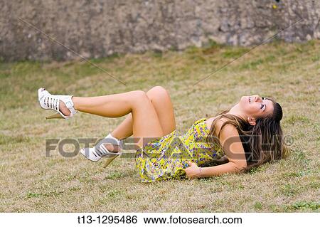 Stock Photograph - Playful lying on her back on the grass young woman. Fotosearch