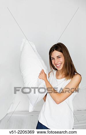 Playful young woman fighting with pillow in bed View Large Photo Image Stock Photo - Playful young woman fighting with pillow in bed. Fotosearch