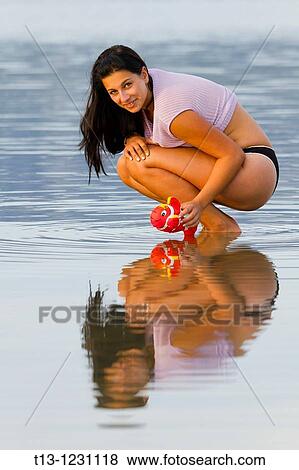 Stock Photo - Playing with a small toy fish young woman in a shallow water. Fotosearch