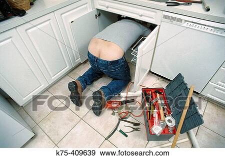 Stock Photo - plumber under kitchen sink. Fotosearch