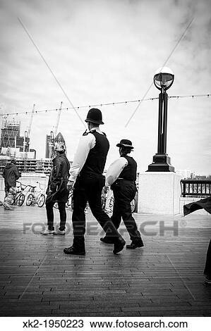 Stock Image - Policeman and policewoman patrol London, near city hall in Thames river path.. Fotosearch