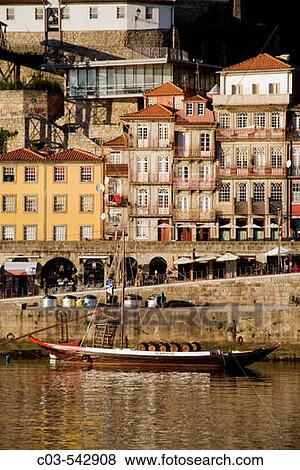 Stock Photo - Porto, Portugal: Ancient-looking boat with empty casks of port wine advertises port-wine tasting lodges on south bank of the Rio Douro. The north bank of the city is in background.. Fotosearch