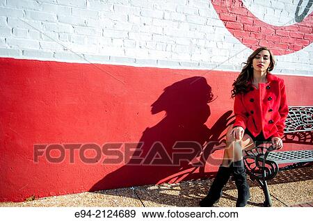 Portrait of a 19 year old brunette woman wearing a red jacket and a short black dress sitting on the arm of a bench in the bright sun with her eyes closed. View Large Photo Image Stock Photo - Portrait of a 19 year old brunette woman wearing a red jacket and a short black dress sitting on the arm of a bench in the bright sun with her eyes closed.. Fotosearch